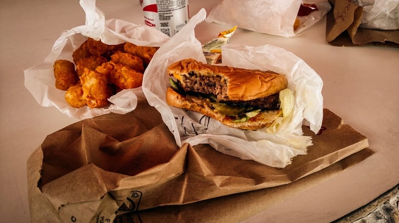 A half-eaten burger and tater tots in paper bags on a table, ready for takeout.