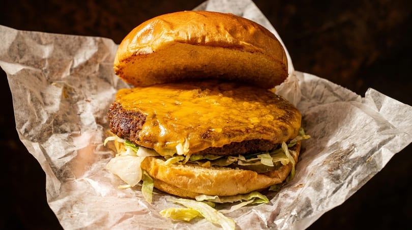 A juicy cheeseburger with melted cheese, lettuce, and a toasted bun, wrapped in white paper.